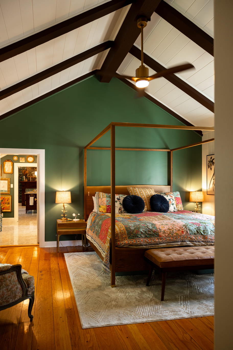 Bed with canopy bed frame in bedroom with vaulted ceilings, white and green walls, and wood floor