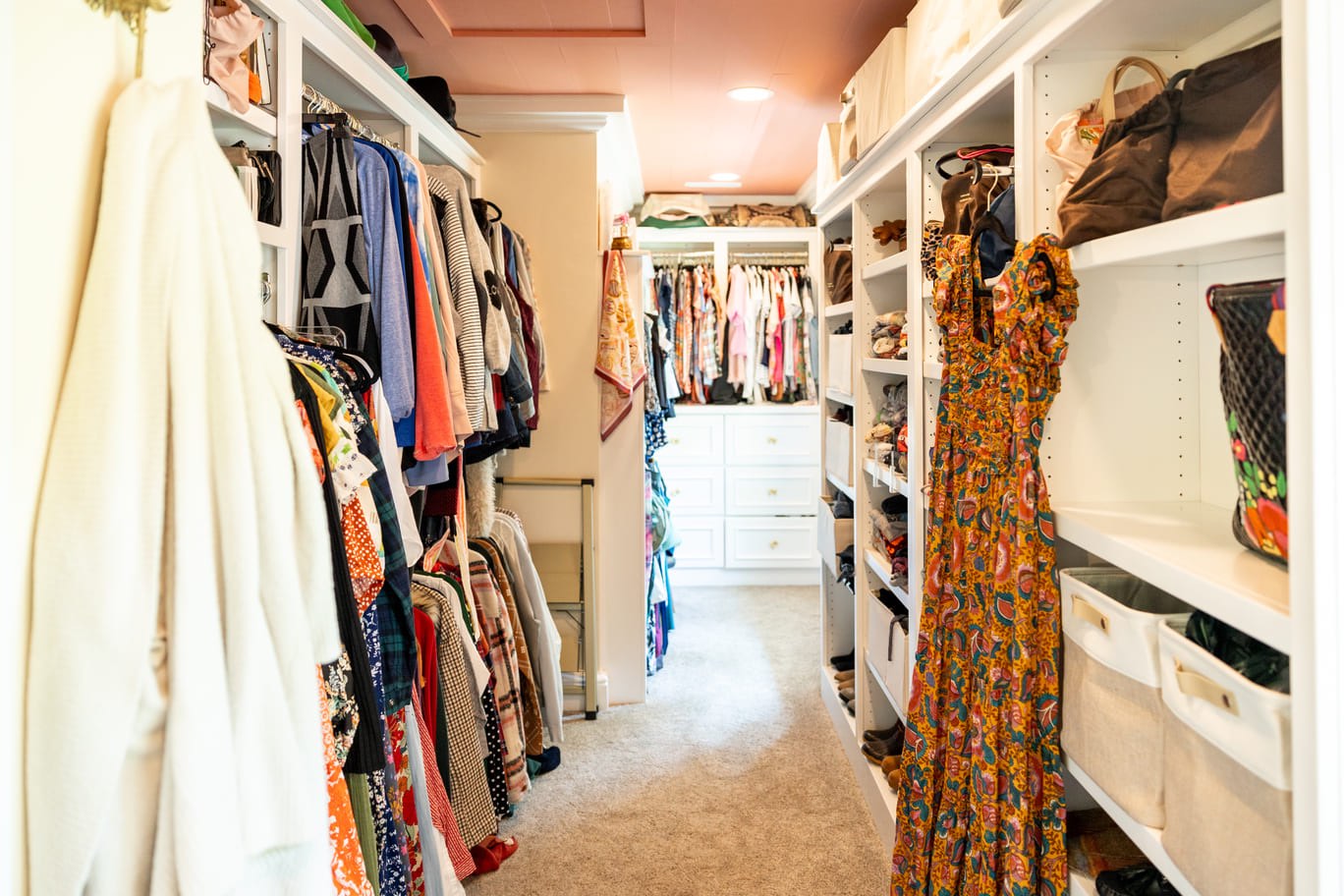 Bright walk-in closet with white custom cabinetry and peach colored ceilings 