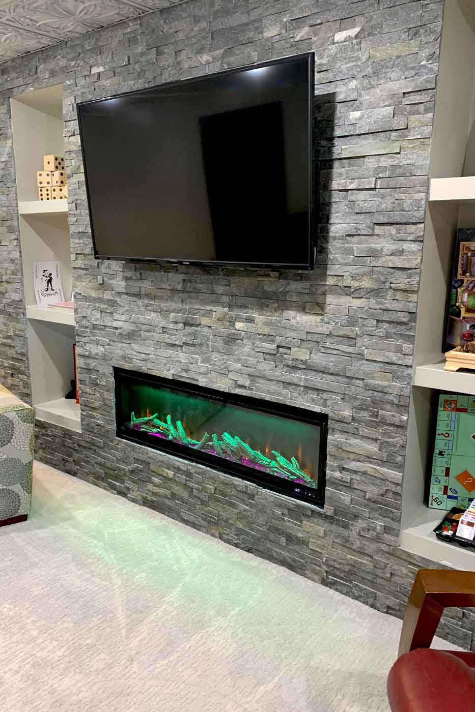 basement with electric fireplace, stone wall, & mounted tv by True Craft Remodelrs in Illinois